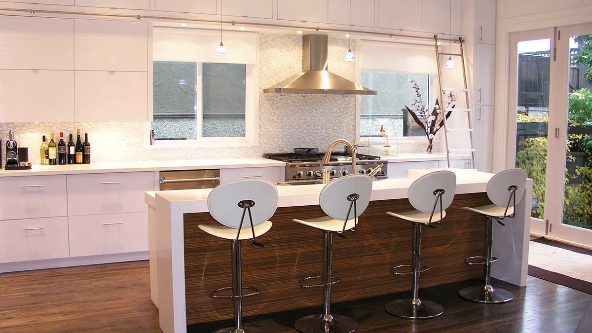 A bright kitchen with a long stone island and timber detailing